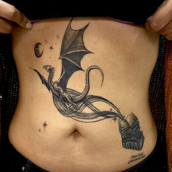 Dragon flying from books stomach tattoo with "I have lived a thousand lives" lettering by Diya Tattoo, Kathmandu