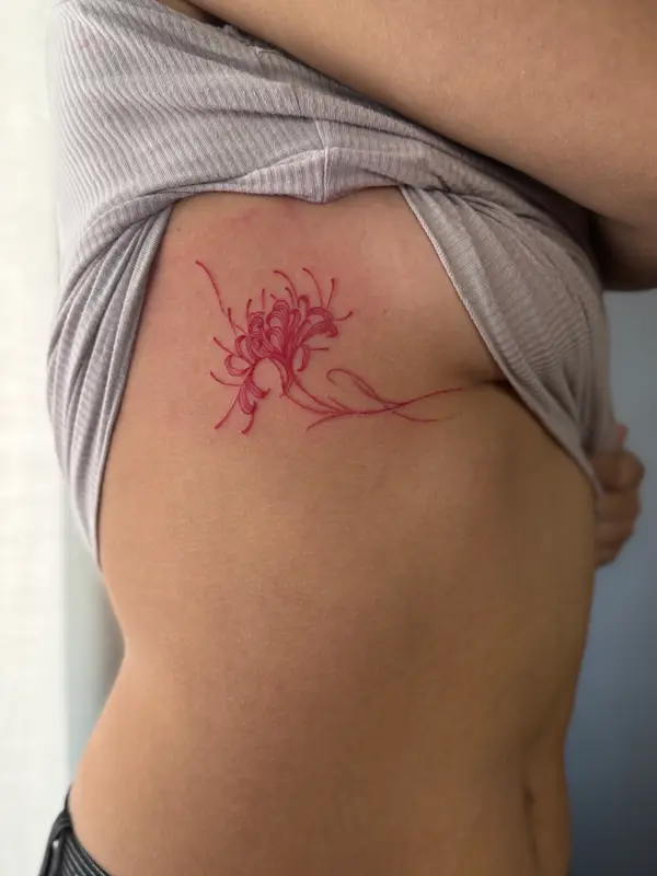 Minimalist red ink spider lily rib tattoo for women by female tattoo artist Diya, Kathmandu
